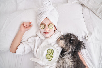 Child with facial mask relaxing on bed with dog during spa sessi