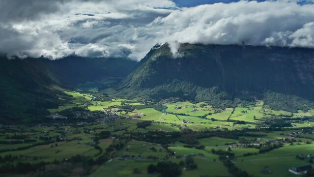 White clouds whirl above the green Norvegian valley between the mountains. Timelapse video