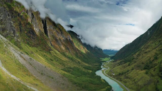 A a wild river flows through the green summer valley between the mountains. A road follows the river. Aerial view.