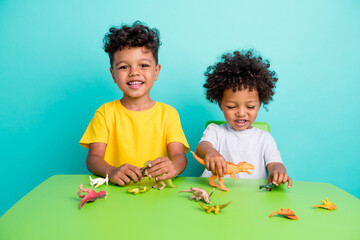 Full length photo of charming schoolboys playing dinosaurs toys sit green table wear trendy garment...