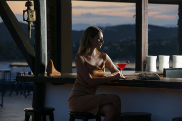 Side view of stylish woman drinking cocktail at the bar counter