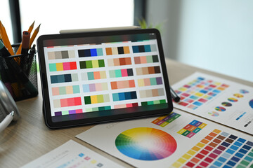 Creative designer, Graphic at workspace with digital tablet, color swatch samples and pencil holder on wooden table.