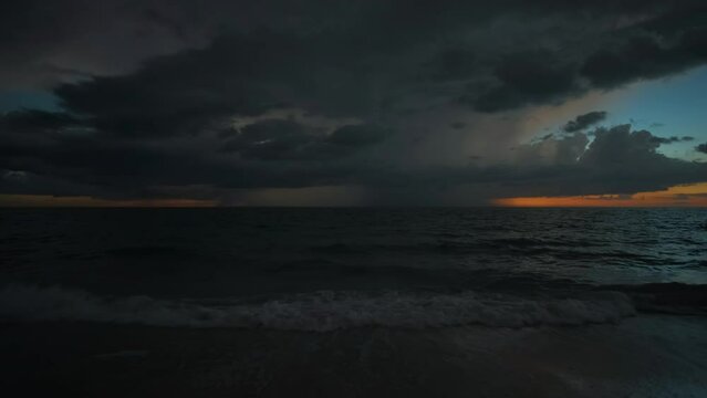 Sunset landscape of dark ominous rainstorm with lightning and thunder over sea water waves crushing on sandy beach. Beautiful seascape in evening