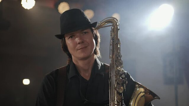 Man with saxophone. Attractive man in hat looking at camera and holds large golden-colored saxophone. Portrait of jazz musician saxophonist on stage