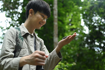 Male hiker using compass for directions in the forest, enjoying his active vacation.