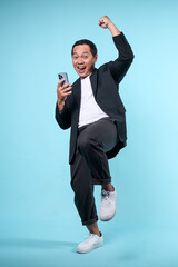 Full body portrait of adult Asian man showing excited gesture while looking to the mobile phone...