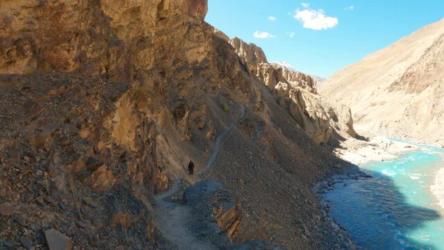 4K shot of an Indian man walking on the hiking trail towards the Phugtal monastery besides the blue Tsarap chu river at Zanskar valley in Ladakh, India. Man trekking towards the Phugtal gompa.