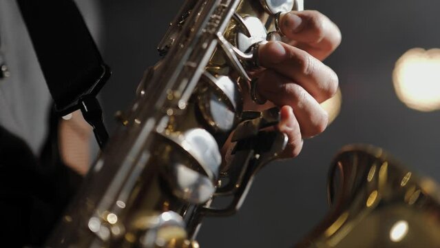 Saxophone. Close-up of saxophone buttons and saxophonist fingers against stage light. Musician plays melody on saxophone