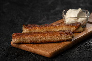 Fried pancakes with sour cream on a wooden board. Dark background