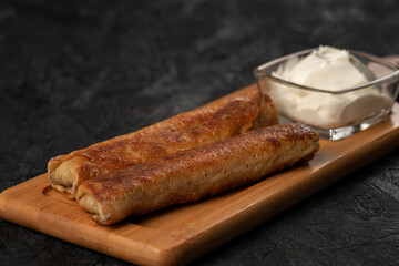 Fried pancakes with sour cream on a wooden board. Dark background