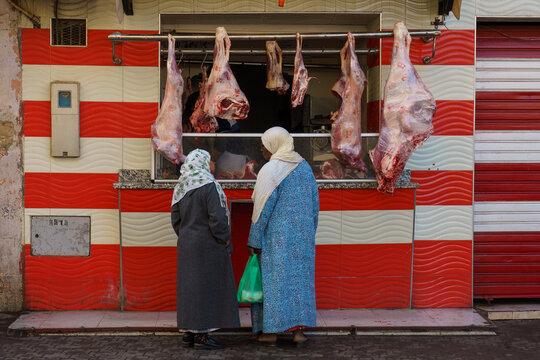 Morocco. Taroudant. Two women in traditional dress in front of a storefront of a butcher's shop