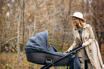 Fototapeta premium Young mother walking with baby stroller and her newborn child in park