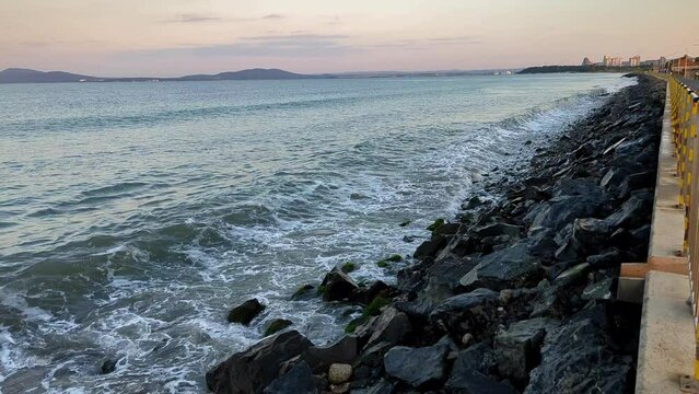 The sea and waves break against the stones in the evening on the embankment, a walking area near the sea.