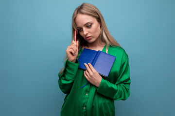 a young woman thoughtfully lowered her head at work holding a notebook and a pencil on a blue...