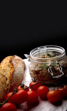 Rustic composition with pate in a jar, red cherry tomatoes and crispy bread on a black background.