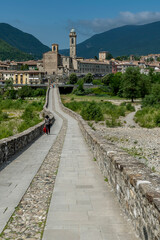 The ancient Ponte Gobbo over the Trebbia river with Bobbio in the background, Italy - obrazy, fototapety, plakaty