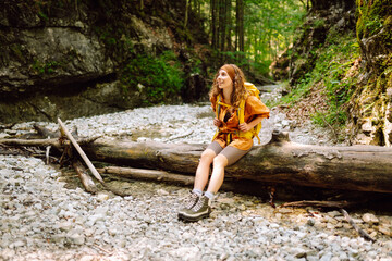 A traveler woman  with a yellow hiking backpack walking along a hiking trail through a forest thicket in the mountains. The concept of travel, hiking. Active lifestyle.