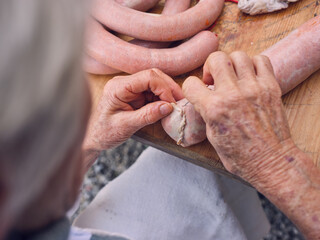 Crop senior woman sewing sausage casing of pork guts