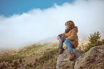 Boy in warm clothes observing nature from boulder © ADDICTIVE STOCK CORE