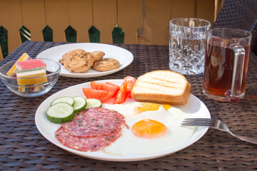 Featuring fried eggs, salami, marmalade, cookies and tea. A close-up photograph of a breakfast.