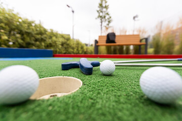 Mini-golf clubs and balls of different colors laid on artificial grass