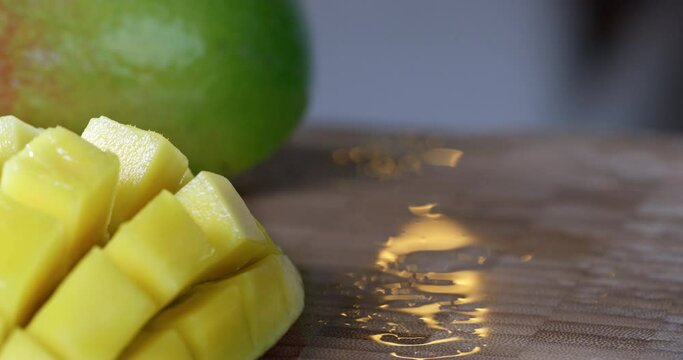 A mango halved, sliced ​​and turned inside out is presented in front of a whole mango.