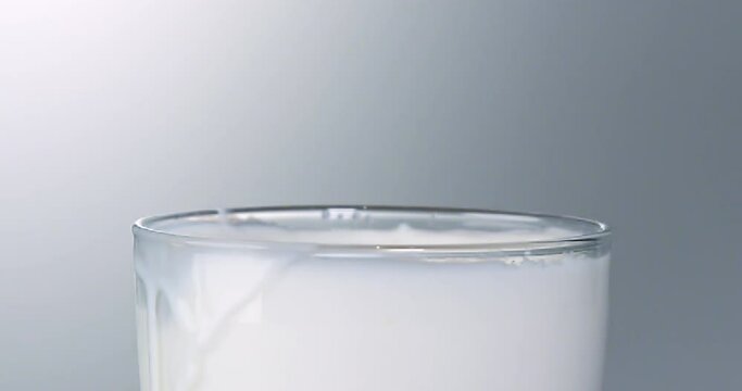 A cookie (Oreo) falls into a glass of milk and splashes a lot.