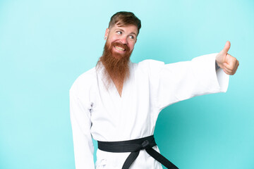 Redhead man with long beard doing karate isolated on blue background giving a thumbs up gesture