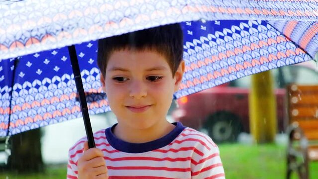 A six-year-old little boy stands outside under an umbrella in the summer.