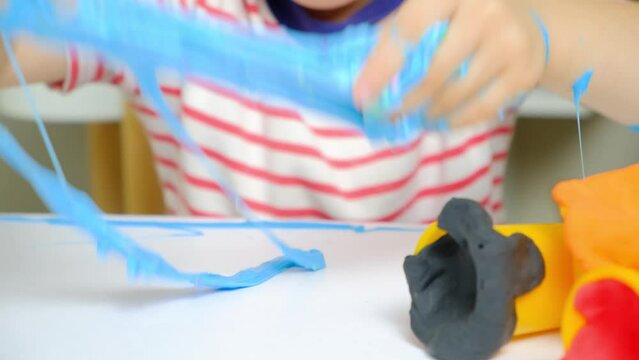 A six-year-old boy plays with slime while sitting at a table at home. A toy for the development of fine motor skills and creativity in children