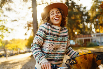 Smiling young woman in a hat and a stylish sweater with a bicycle walks and enjoys the autumn...