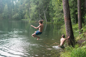 boys jumps into the water using a tarzan swing while swimming in a forest lake