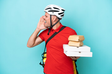Young caucasian man with thermal backpack and holding fast food isolated on blue background shouting with mouth wide open to the side
