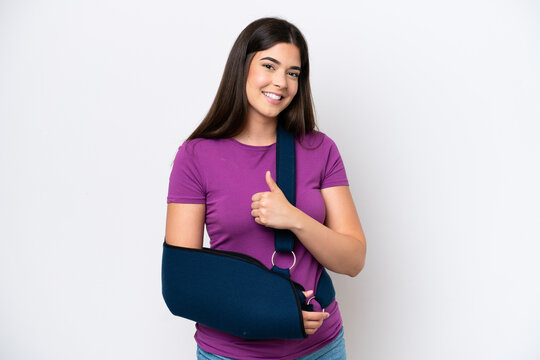 Young Brazilian woman with broken arm and wearing a sling isolated on white background giving a thumbs up gesture