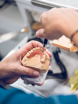 Crop dental technician carving denture while working in lab
