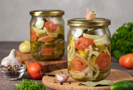 Pickled cucumbers salad with tomatoes and sweet peppers in two jars on gray background, Closeup