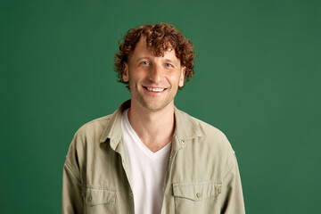 Obraz na płótnie Canvas Happiness. Portrait of mature man with curly hair, in casual clothes posing with smile against green studio background. Concept of human emotions, facial expression, lifestyle, fashion, ad