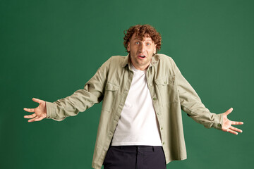 Mature curly man in casual clothes standing with astonished face, posing against green studio background. Concept of human emotions, facial expression, lifestyle, fashion, ad