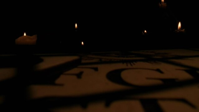 Macro shot of a planchette laying on the side of the ouija board in bright flashing lights. Ouija boeard session. Blurred candles on the background.