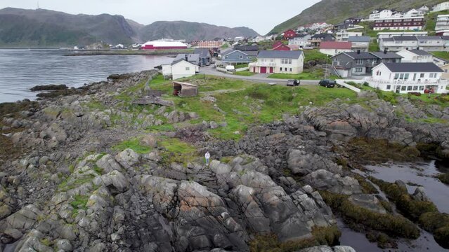 Aerial shot of rocks by the water with people taking pictures with a village and a fjord in the background