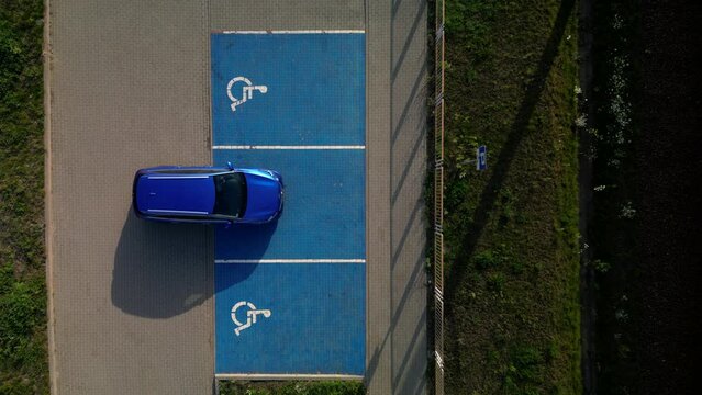 Outdoor car parking places with handicapped symbol icons. Parking places reserved for disabled person. Blue car between parking places. Aerial drone top down vertical view..