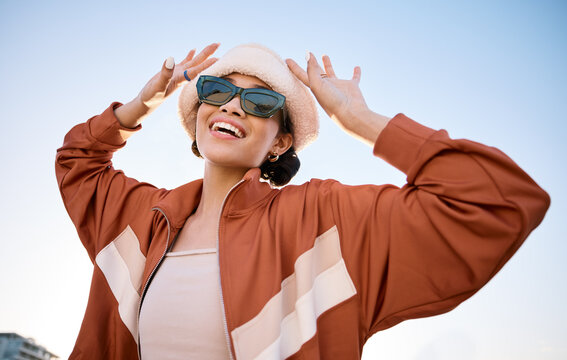 Fashion, sunglasses and smile with a trendy woman outdoor on a blue sky for freedom, energy or style. Portrait, summer and clothes with a happy young model in an urban outfit while on vacation