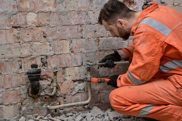 Plumber repairing leaking water connection. Plumber wearing orange coveralls and gloves.