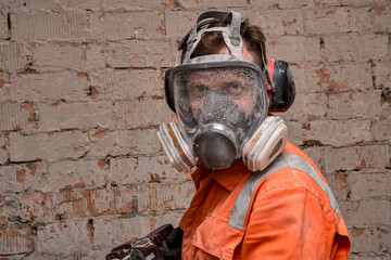 Builder wearing full face respirator mask and ear defenders for working in dusty and noisy environment. 