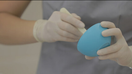 Close-up of the hands of a beautician in gloves holding a blue bowl with dental floss