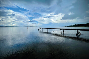 Blue sky with white clouds. Beautiful beach with a long bathing jetty. Calm sea and stunning cloud formations. 