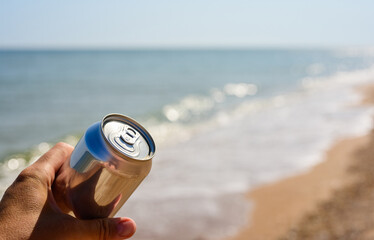 An aluminum can in the hand of a tourist against the backdrop of the sea. Close-up, selective focus.