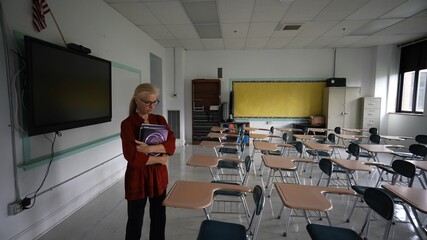 Sad unhappy teacher in large empty classroom with the lights turned off during budget cuts or a...
