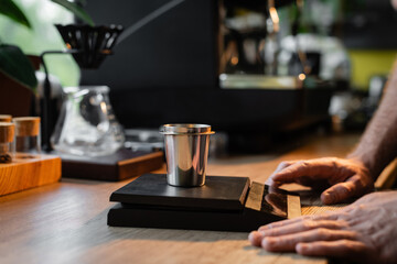 Fototapeta na wymiar cropped view of barista standing near beaker on electronic scales near coffee machine in cafe