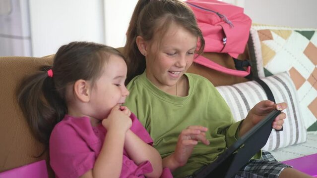 Two Little Sister are Sitting on the Coach and Using a Digital Tablet